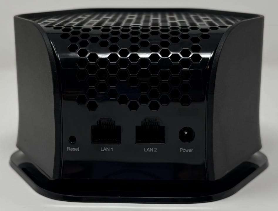 A compact black electronic device with a hexagonal vent pattern covering the top portion of the device descending to the middle section of the back panel of the device. Directly below the vent are two labelled ethernet ports marked as LAN 1 and LAN 2. Directly to the left of these ports is a small recessed reset button. Directly to the right of the Ethernet ports is a circular power input labelled power.