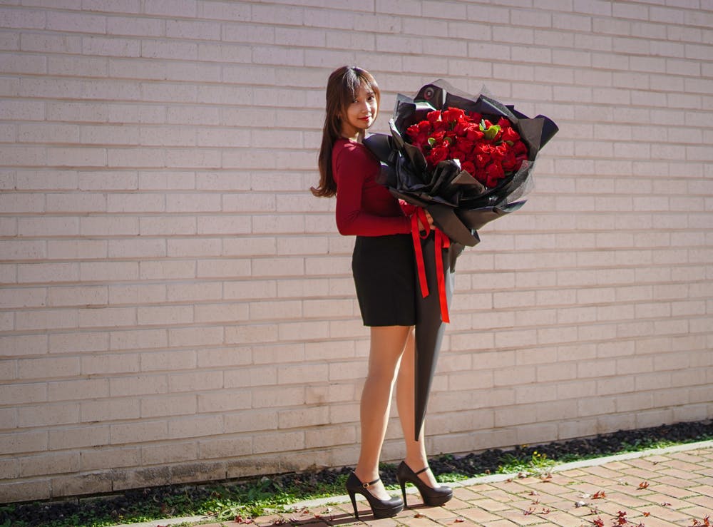 벽돌 벽 앞에서 빨간 장미 꽃다발을 들고있는 여자