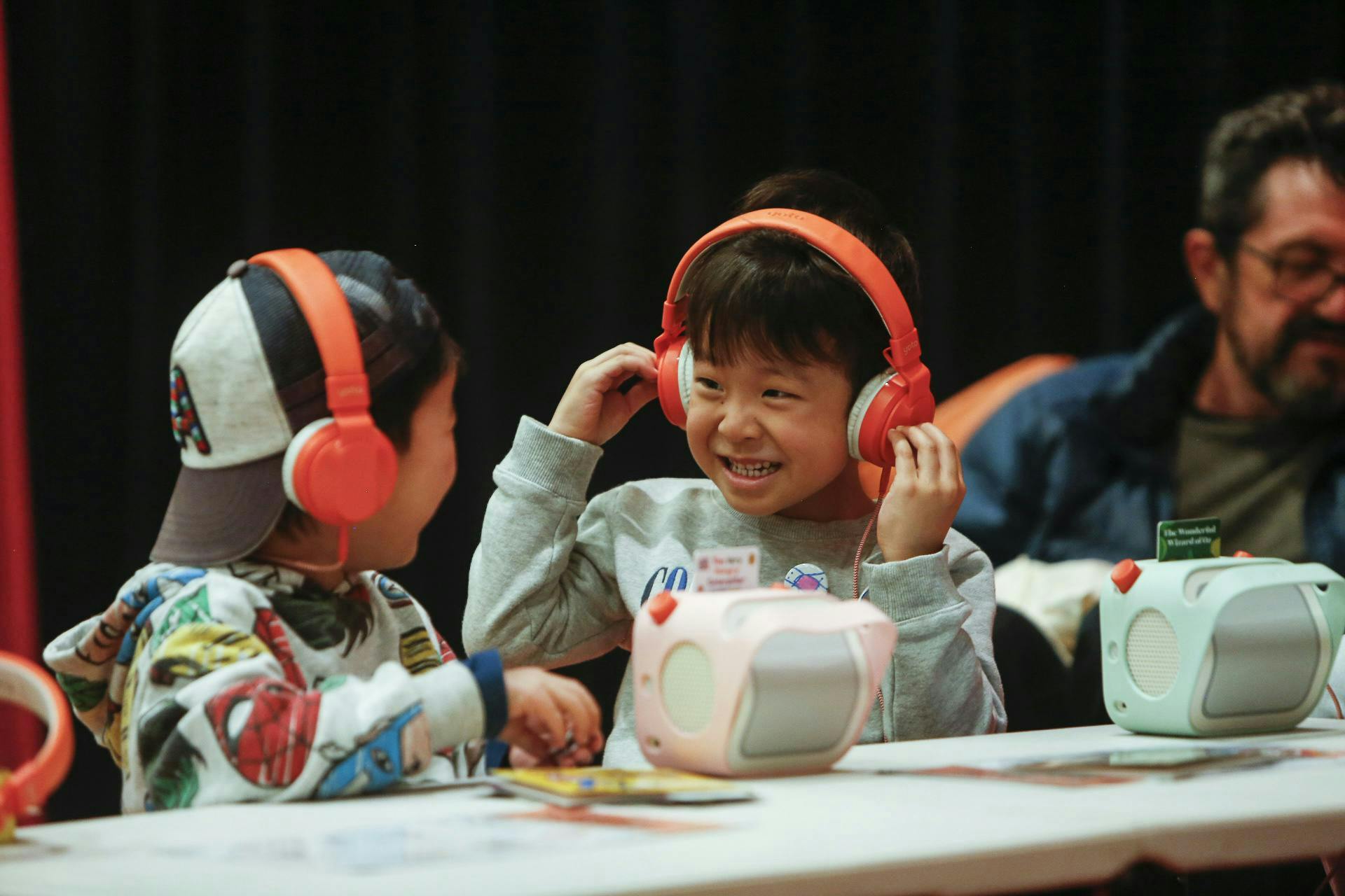 Two kids wearing Yoto headphones, smiling at each other while listening to cards in Yoto Players