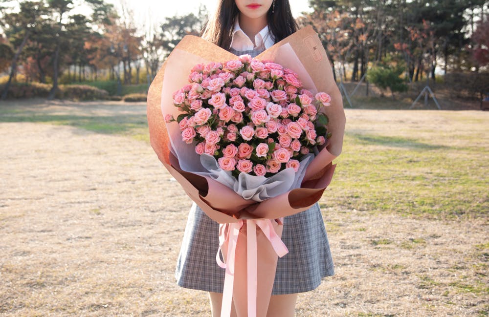 공원에서 분홍색 장미 꽃다발을 들고있는 소녀