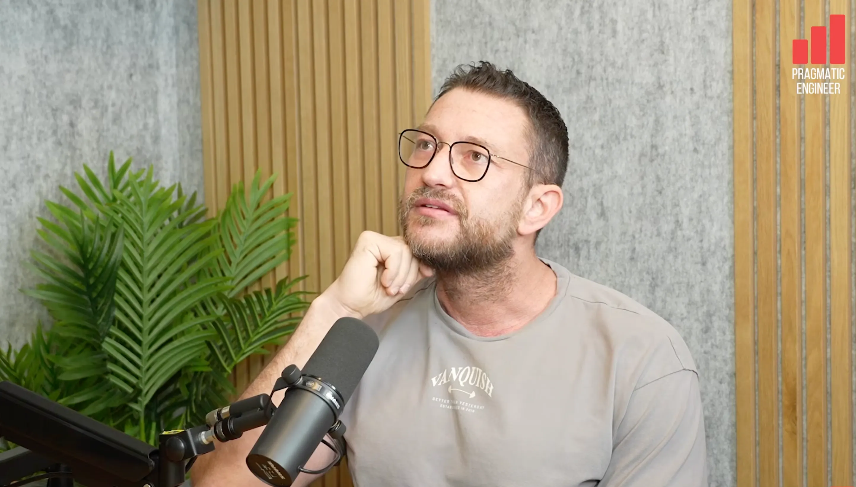 안경을 쓴 남자가 마이크 앞에 앉아 있다