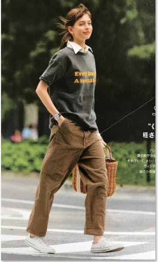 여자가 갈색 바지와 t- 셔츠를 입고 길을 건너고 있습니다.