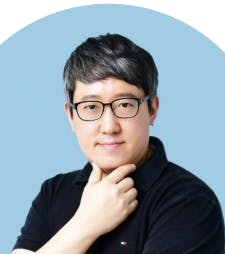 안경을 쓴 남자가 턱에 손을 얹고 포즈를 취하고 있다